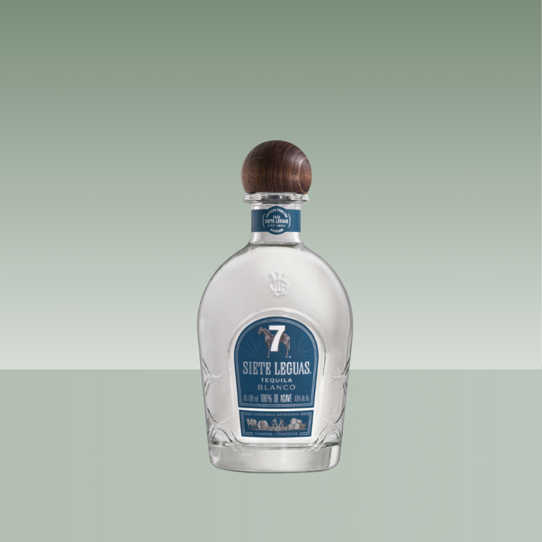 Botella de tequila Siete Leguas Blanco, de vidrio transparente con tapón de madera y etiqueta azul frontal.