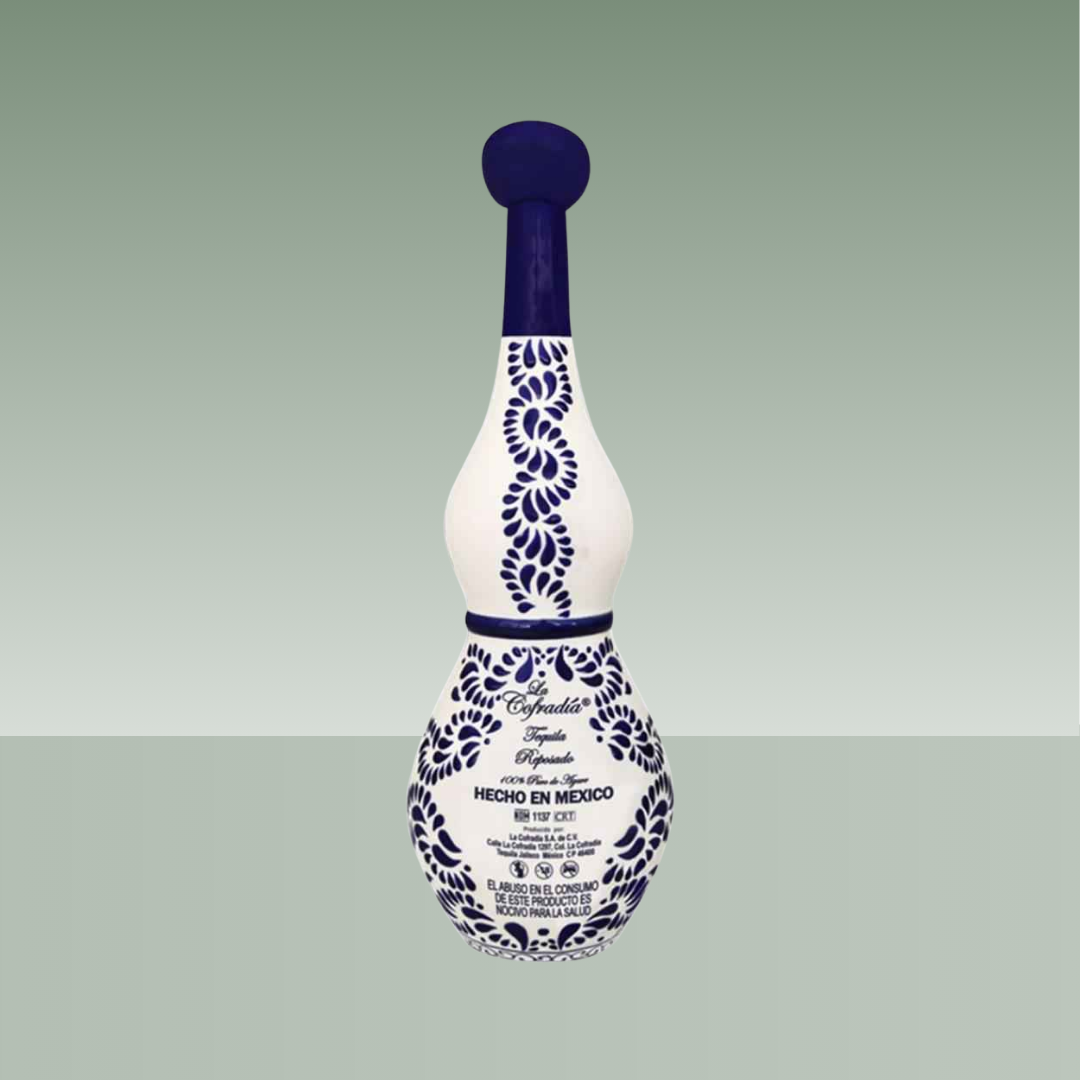 Vista trasera de botella artesanal de cerámica blanca con decoración azul cobalto, motivos vegetales pintados a mano y tapón cerámico, con texto serigrafiado en la parte inferior.