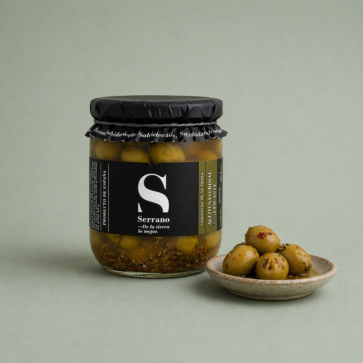 Tarro de aceitunas verdes aliñadas Serrano con especias y aceitunas servidas en un plato.