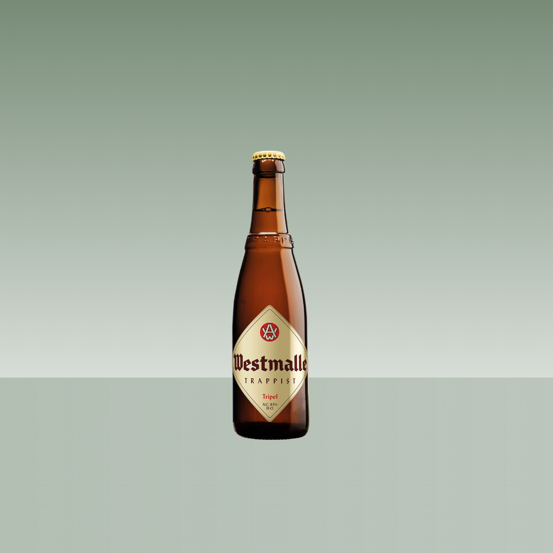 Botella de cerveza belga Westmalle Trappist Tripel, de vidrio ámbar con etiqueta clásica en tonos crema y rojo, presentada sobre fondo neutro verde suave.