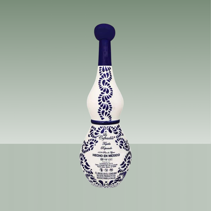 Vista trasera de botella artesanal de cerámica blanca con decoración azul cobalto, motivos vegetales pintados a mano y tapón cerámico, con texto serigrafiado en la parte inferior.
