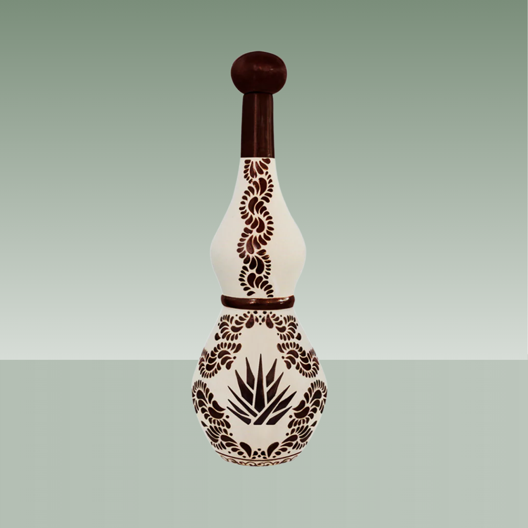 Botella de tequila de cerámica artesanal decorada a mano en tonos crema y marrón, con motivos vegetales y agave, cuello alargado y tapón cerámico.