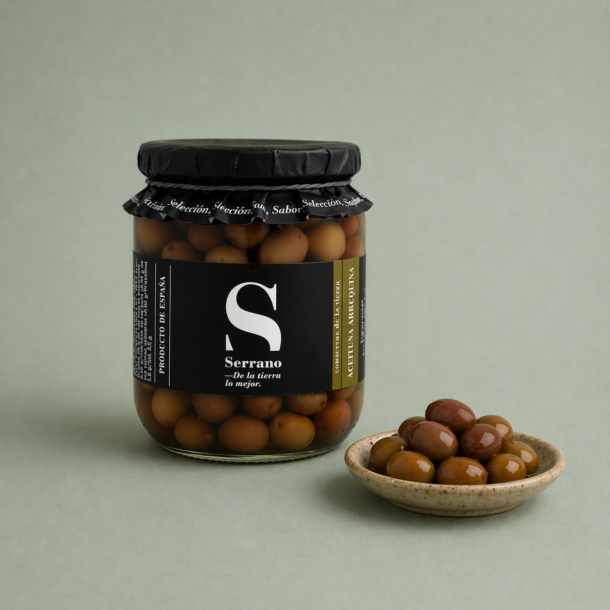 Tarro de aceitunas arbequinas Serrano con aceitunas servidas en un plato pequeño.