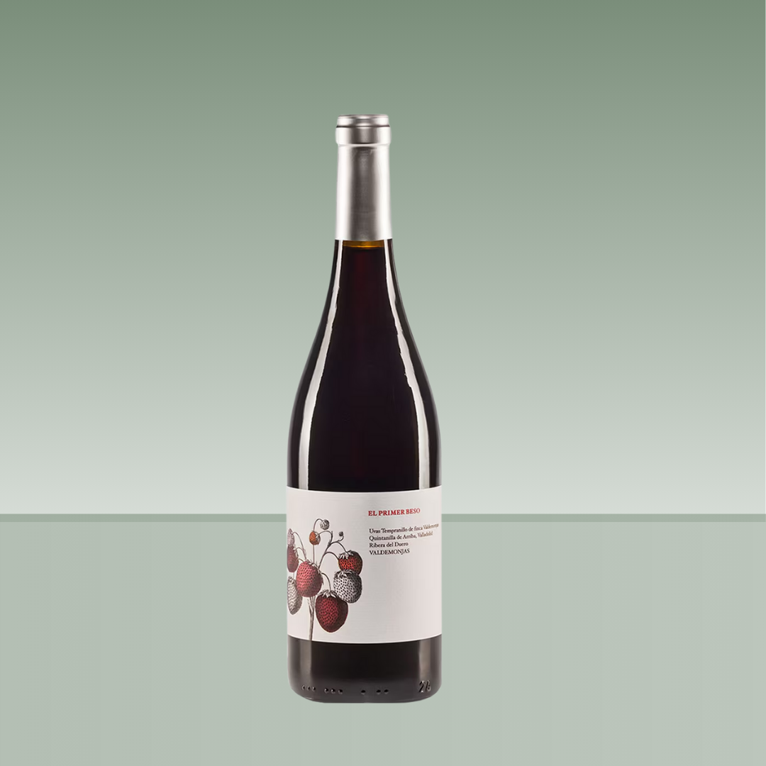 Botella de vino tinto "El Primer Beso", con cápsula plateada y etiqueta blanca ilustrada con fresas en tonos rojos y negros, sobre fondo verde claro.